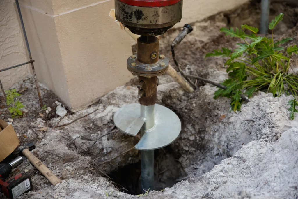 Helical pier installation in progress using hydraulic equipment to stabilize a foundation.